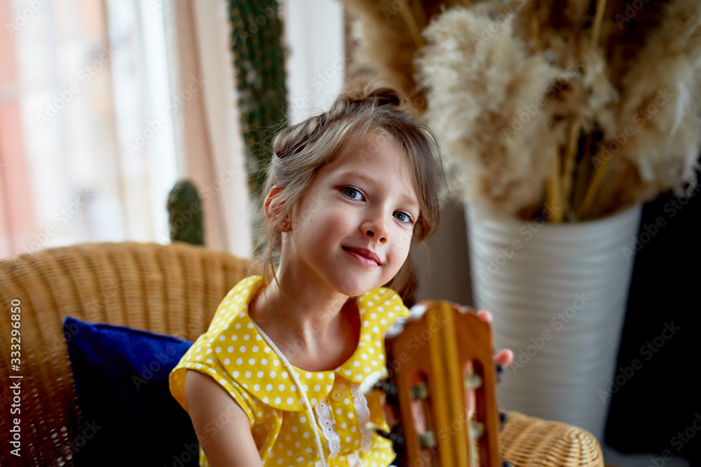 Fototapeta premium Portrait of a smiling girl in a yellow dress 6 years old. Pierced ear. Blue eyes, long hair.