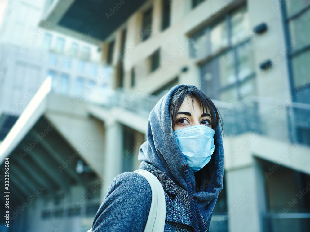 woman in hood with face mask for protection of coronavirus in city, modern building on background. Concept coronavirus pandemic, SARS, MERS, COVID-19, quarantine, isolation period.