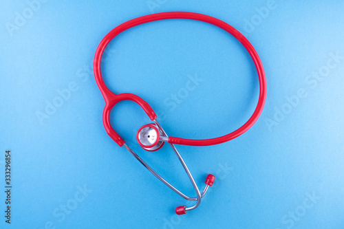Close up isolated of red stethoscope in round shape on light blue background with a place for text. Medical mockup or template.