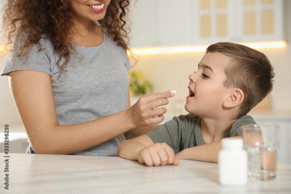 African-American woman giving vitamin pill to little boy in kitchen African-American woman giving vitamin pill to little boy in kitchen