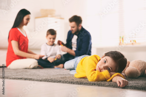 Unhappy little girl feeling jealous while parents spending time with her brother at home