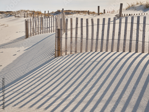 Fototapeta Naklejka Na Ścianę i Meble -  Long late afternoon shadows highlight the thin wooden slats of the storm fencing found in New Jersy Island Beach State Park to protect the sand dunes from wind wave and human erosion