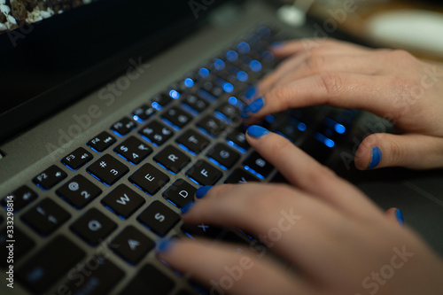 Kobieta pisze maila na klawiaturze laptopa (komputera). Przyciski mają niebieskie podświetlenie