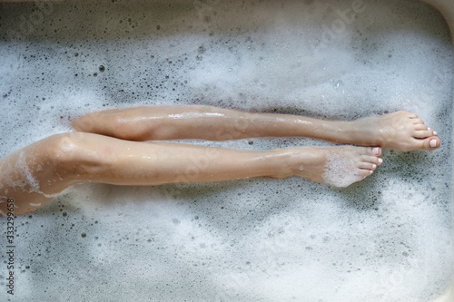 Young adult girl taking bath holding legs over foam water