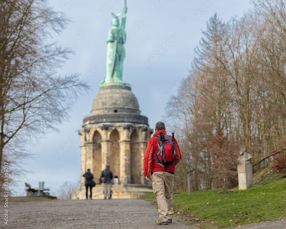 Obraz premium A hiker with a backpack and hiking poles in winter in Germany. The man approaches the Hermann Monument, which is near the Westphalian city of Detmold.