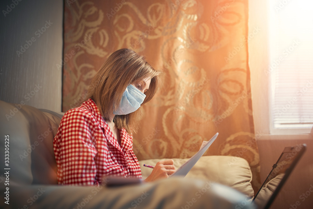 Young businesswoman in a medical protective mask works from home at the computer during self-isolation and quarantine. Virus coronavirus outbreak, flu epidemic and covid ncov novel. Stay home. Young businesswoman in a medical protective mask works from home at the computer during self-isolation and quarantine. Virus coronavirus outbreak, flu epidemic and covid ncov novel. Stay home.