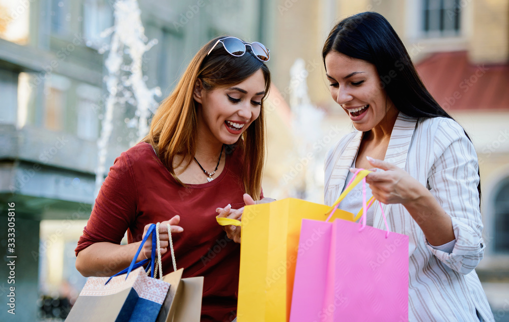 Shopping time. Beautiful women take a break in the city park after shopping. Consumerism, lifestyle concept Shopping time. Beautiful women take a break in the city park after shopping. Consumerism, lifestyle concept