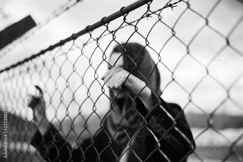 The migrant is holding his hands behind the protective fence
