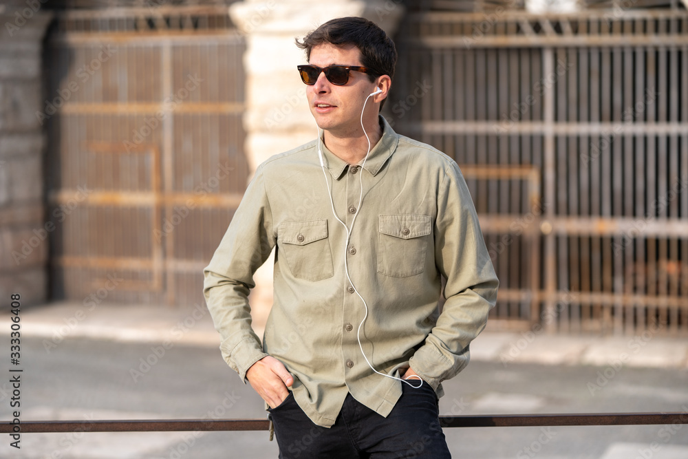 Portrait of young smiling man isolated on outside outdoor background listeling music with headphones Portrait of young smiling man isolated on outside outdoor background listeling music with headphones