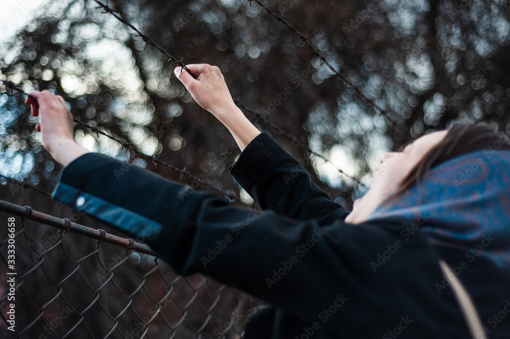 The migrant is holding his hands behind the protective fence The migrant is holding his hands behind the protective fence