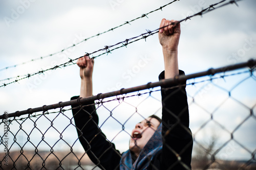 The migrant is holding his hands behind the protective fence © Zoran