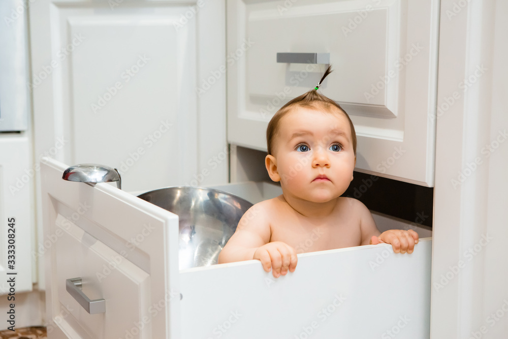 Happy baby girl smiling sitting in kitchen drawer with pans Happy baby girl smiling sitting in kitchen drawer with pans