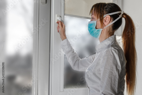 a woman in a medical mask opens a window for airing. Self-isolation to prevent the COVID-19 coronavirus pandemic.