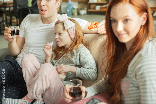 Family spending nice time together at home  looks happy and cheerful. Mom  dad and daughter having fun  eating pizza  relaxing while sitting on sofa. Togetherness  home comfort  love  relations