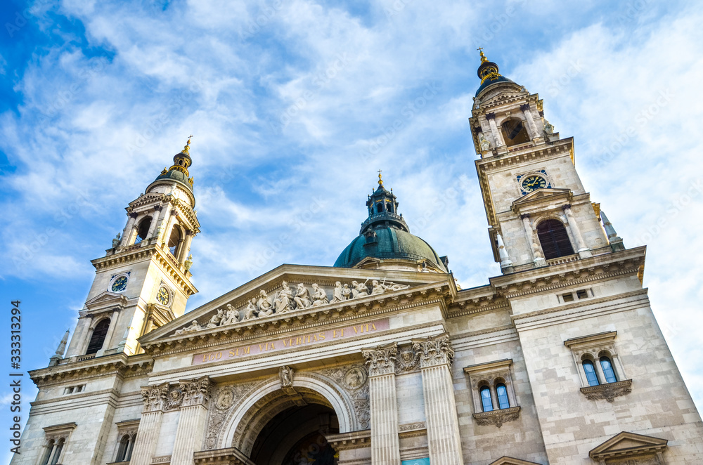 Horizontal picture of the front side facade of Saint Stephen's Basilica in Budapest, Hungary with blue sky and clouds above.Roman Catholic basilica built in neoclassical style. Both towers and cupola