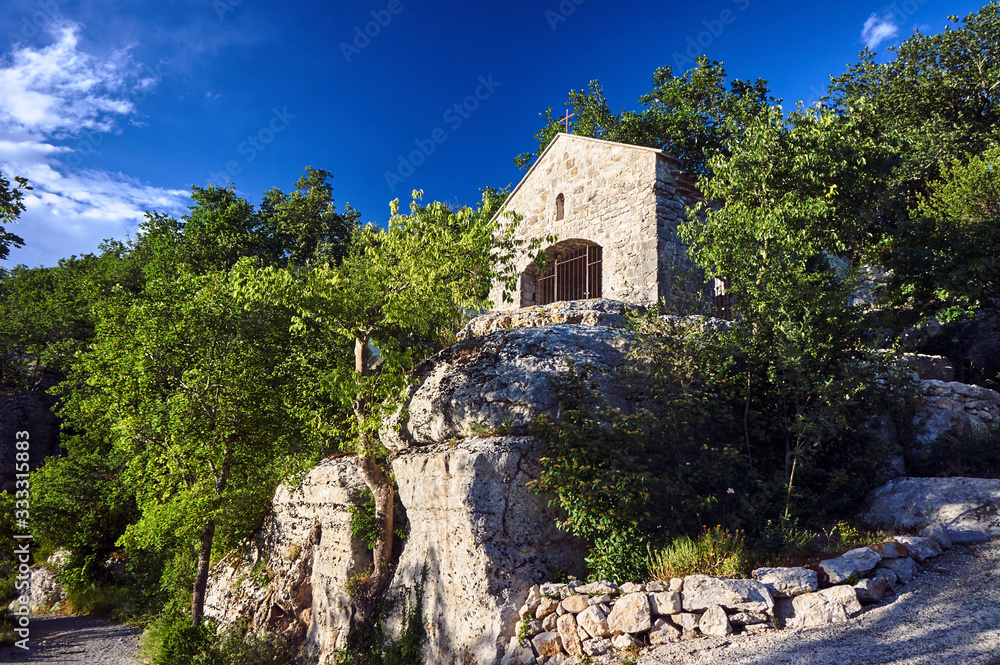 A stone, historic chapel on the rocky slope of a canyon in the Ardeche region in France.