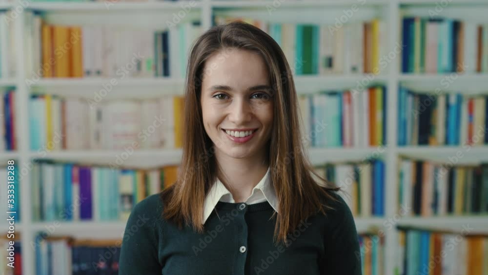 Attractive academic woman teacher or student smiling cheerful near bookshelves enjoying her study in modern library room. Real portrait. Attractive academic woman teacher or student smiling cheerful near bookshelves enjoying her study in modern library room. Real portrait.