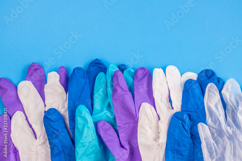 Flat lay composition with different medical multicolor gloves in a row on blue color background. Space for text