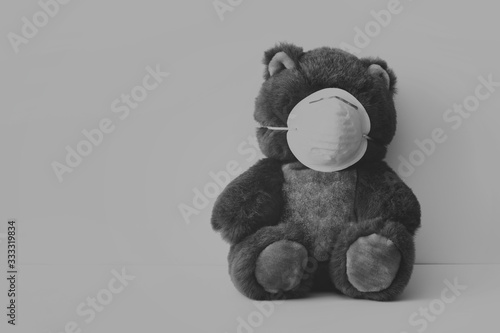 Concept with teddy bear and facial antivirus mask in sad gray dark black colors. Photo with blank space.  photo