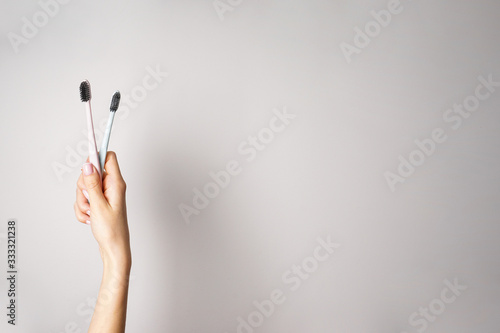 Colored toothbrushes with black bristles in the hands of a young woman on a gray background. Space for text