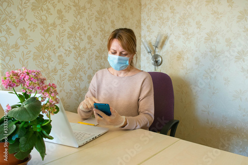 The young woman in the protective mask and gloves works at the computer