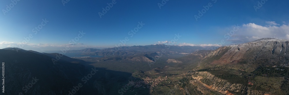 Aerial view of Delphi, Greece at sunrise, the Gulf of Corinth, Morning fog over mountains, hoarfrost on roofs, mountainside with layered hills beyond with rooftops in foreground