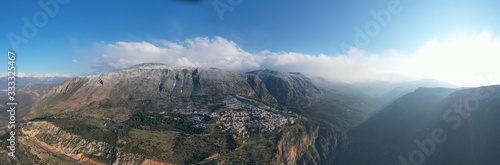 Aerial view of Delphi, Greece at sunrise, the Gulf of Corinth, Morning fog over mountains, hoarfrost on roofs, mountainside with layered hills beyond with rooftops in foreground