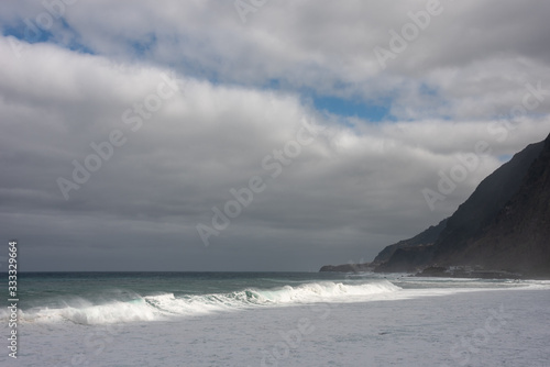Waves on the Atlantic Ocean in Sao Vicente, Madeira Island. Cloudy sky, high hills in the background. 