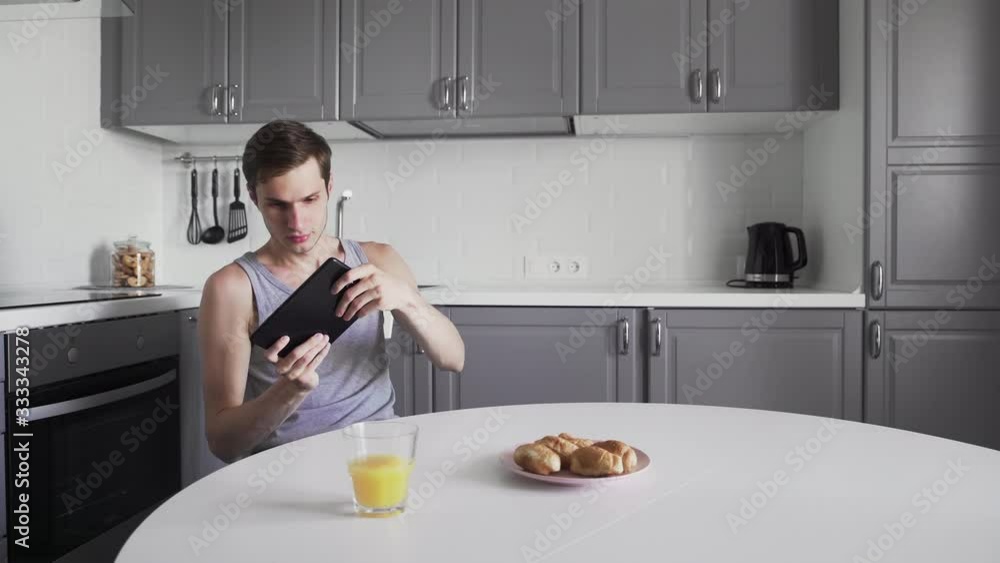 Young man using digital tablet to play video game while sitting in kitchen at home Young man using digital tablet to play video game while sitting in kitchen at home