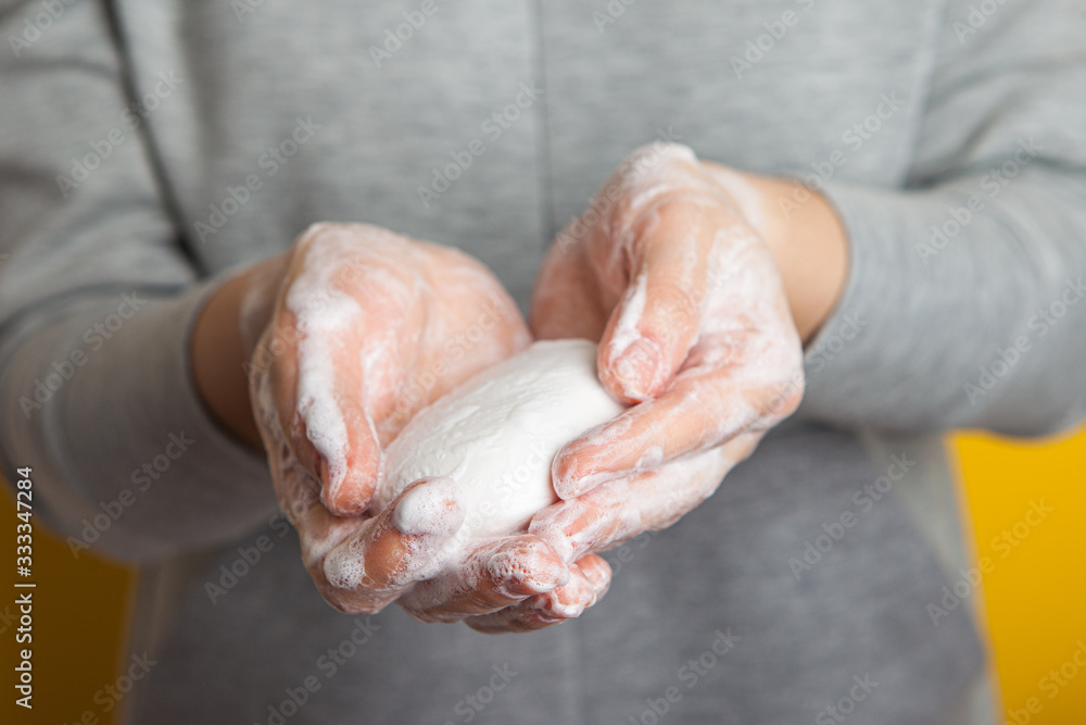 Fototapeta premium woman holds and shows soap in her hands. Palms and fingers in soapy foam stretch the soap forward, on a yellow background. Hand disinfection in the fight against coronavirus.