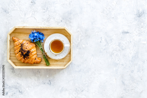 Breakfast with summer flowers. Tea, croissant and cornflowers on light background top-down copy space