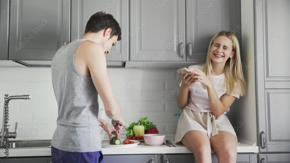 A girl photographs a guy who cuts vegetables for salad for lunch in the kitchen A girl photographs a guy who cuts vegetables for salad for lunch in the kitchen