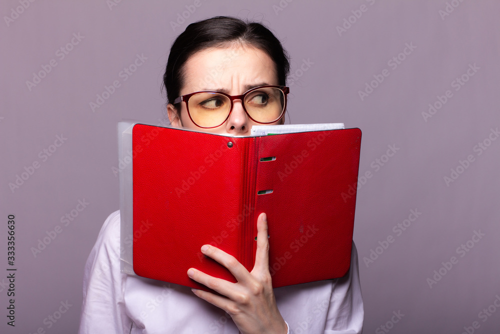 girl in a white shirt and glasses holds a red notebook in her hand girl in a white shirt and glasses holds a red notebook in her hand