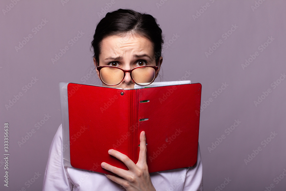 girl in a white shirt and glasses holds a red notebook in her hand girl in a white shirt and glasses holds a red notebook in her hand