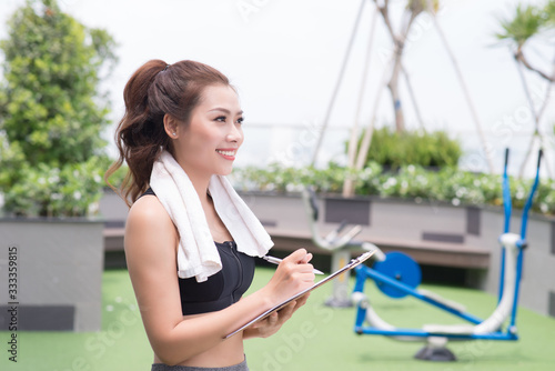 A pretty young asian female fitness trainer taking some notes while at the park