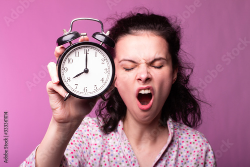  beautiful curly girl in pajamas holds alarm clock in hands, pink background © Диана Шиловская