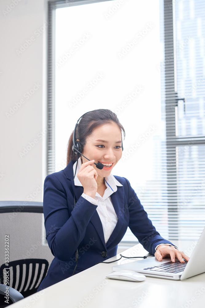 Portrait of happy smiling female customer support phone operator at workplace. Asian