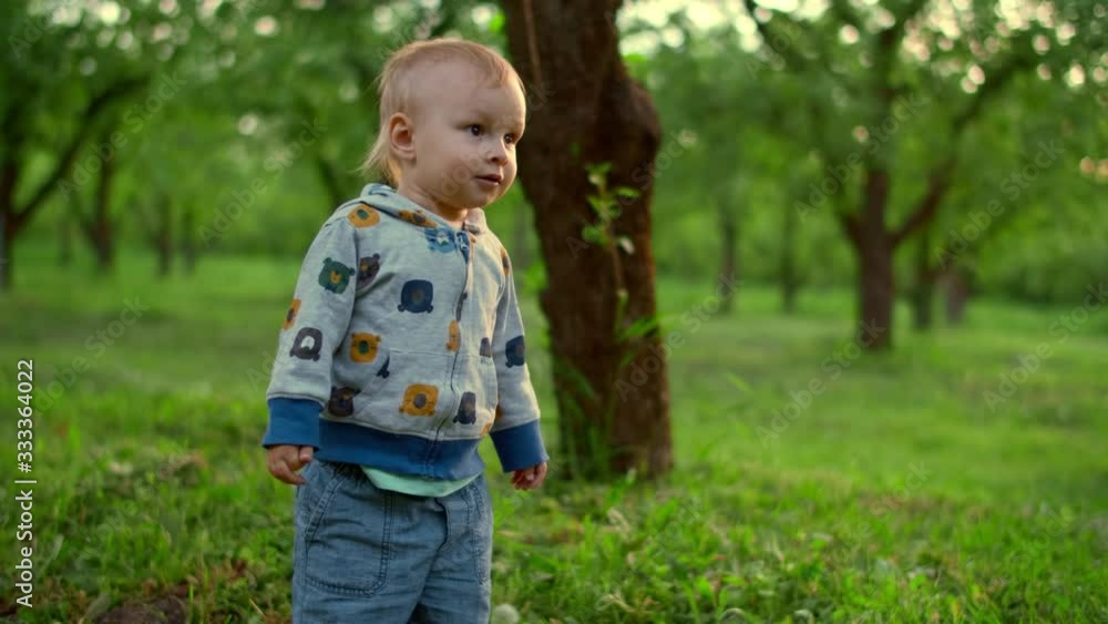 Cute kid boy falling on ground outdoors. Little baby standing in green park. Cute kid boy falling on ground outdoors. Little baby standing in green park.