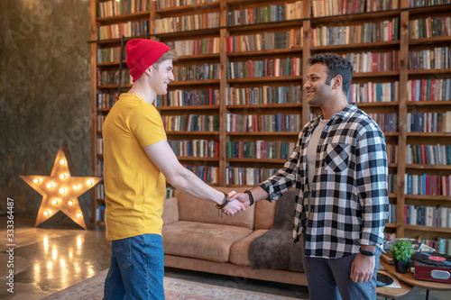 Two young handsome men shaking hands standing in the room