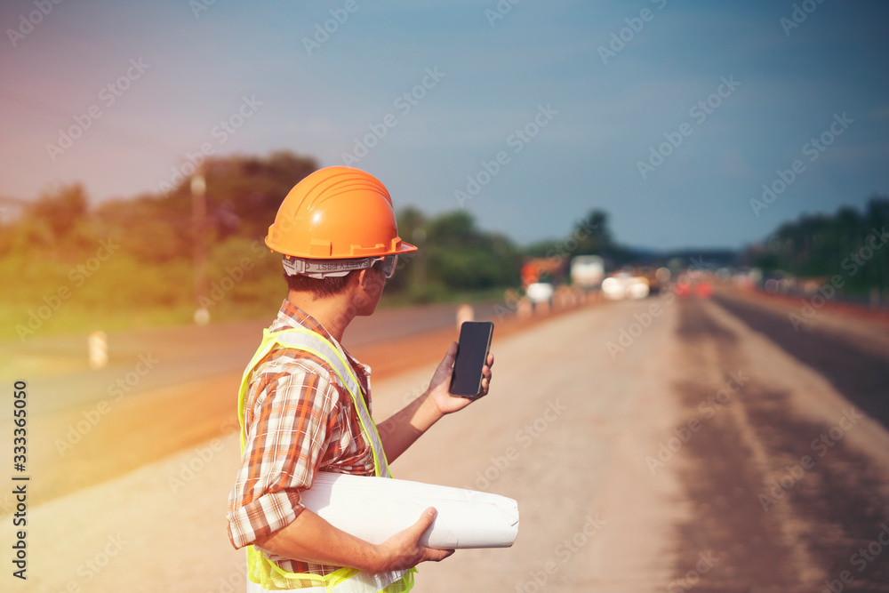 Engineer wear a hard helmet and holding blueprint on road construction site with machinery,safety first concept Engineer wear a hard helmet and holding blueprint on road construction site with machinery,safety first concept