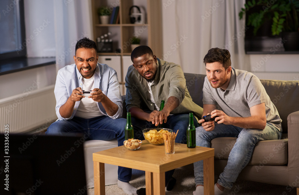 friendship, technology and leisure concept - smiling male friends with gamepads and beer playing video game at home at night friendship, technology and leisure concept - smiling male friends with gamepads and beer playing video game at home at night