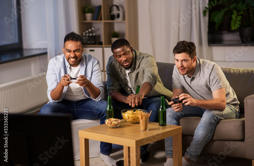 friendship  technology and leisure concept - smiling male friends with gamepads and beer playing video game at home at night