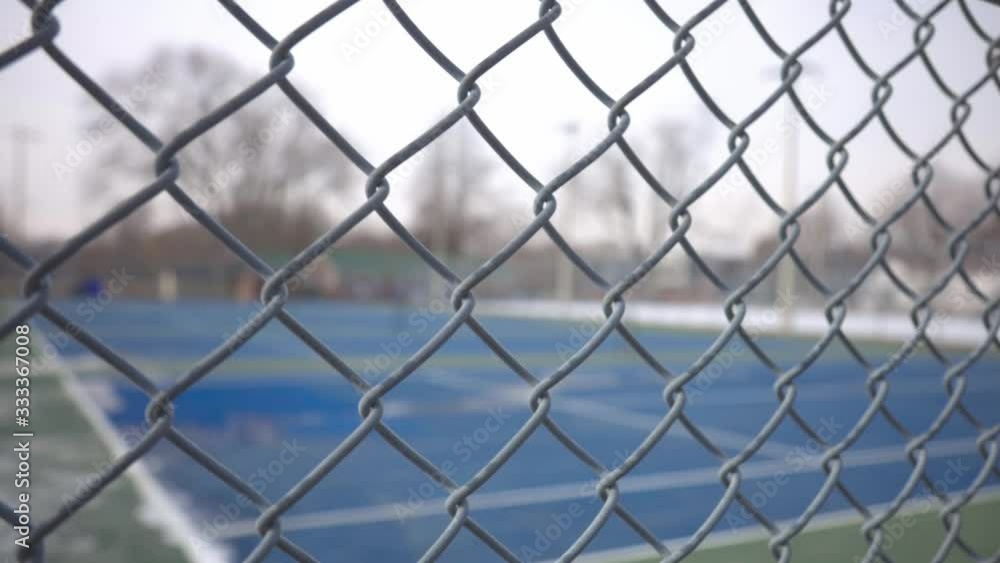 A Wide Metal Of Fence Of Blue Painted Tennis Court Surrounded With Trees. -medium shot A Wide Metal Of Fence Of Blue Painted Tennis Court Surrounded With Trees. -medium shot