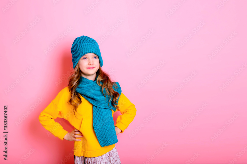 Blonde kid child girl is dressed in a warm sweater, scarf and beanie on a pink background. Fight the cold. Winter and autumn seasons. Concept of children's health, vitamins, medicines. Blonde kid child girl is dressed in a warm sweater, scarf and beanie on a pink background. Fight the cold. Winter and autumn seasons. Concept of children's health, vitamins, medicines.