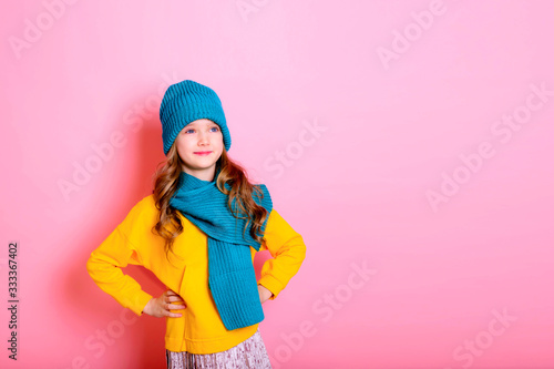 Blonde kid child girl is dressed in a warm sweater, scarf and beanie on a pink background. Fight the cold. Winter and autumn seasons. Concept of children's health, vitamins, medicines.