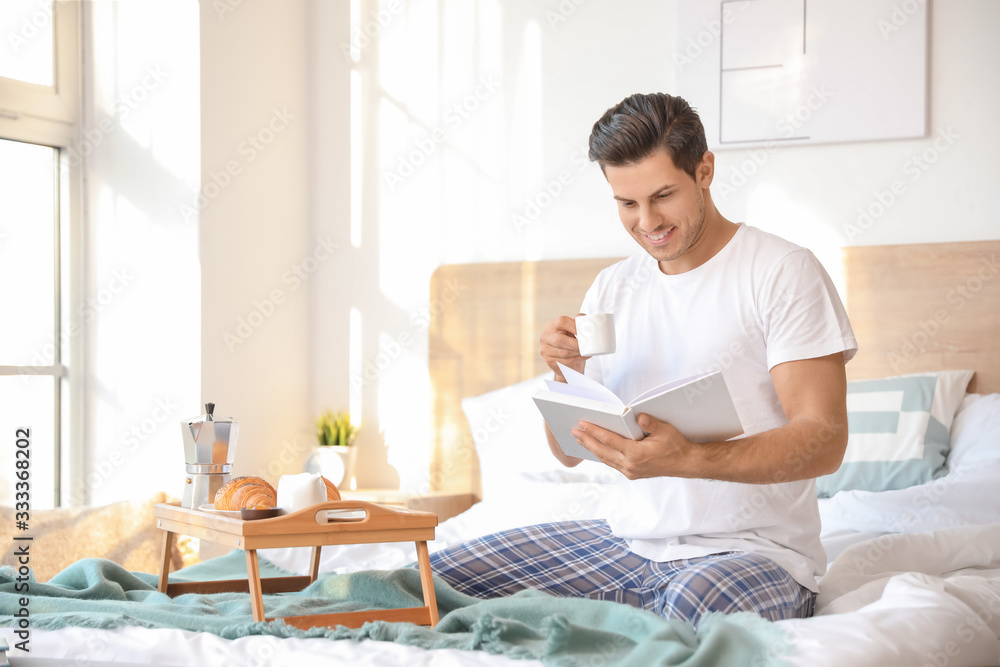 Morning of handsome young man reading book during breakfast in bed Morning of handsome young man reading book during breakfast in bed