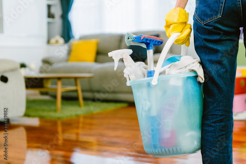 Photography Woman carry bucket full of cleaning products with living room in backgroud