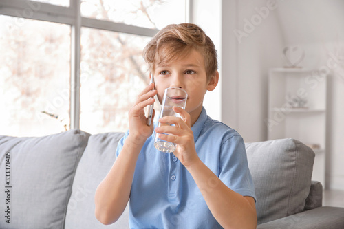 Cute little boy drinking water while talking by phone at home