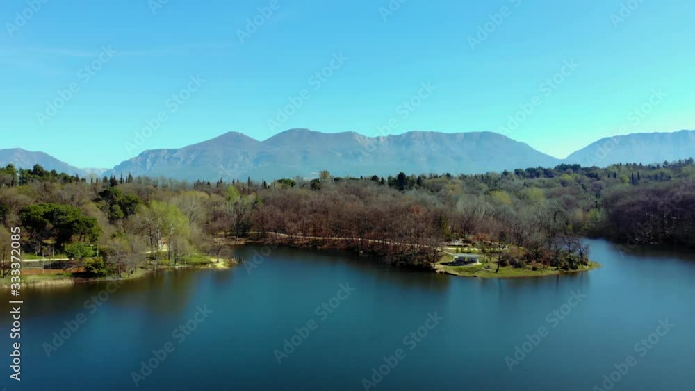 Park with trees forest and green meadows on bank of lake with calm water reflecting bright blue sky in Spring Park with trees forest and green meadows on bank of lake with calm water reflecting bright blue sky in Spring