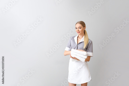 Beautiful young chambermaid with towels on light background